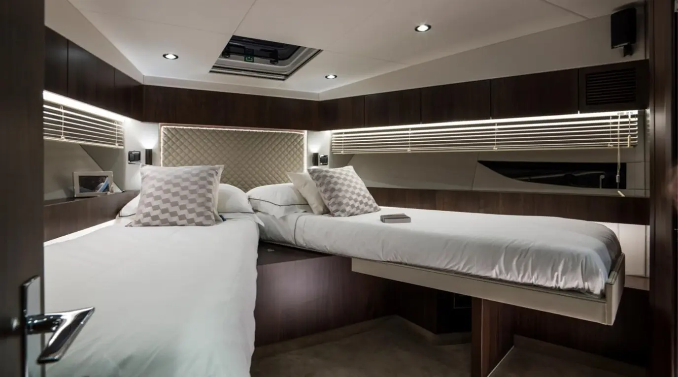 Modern yacht cabin featuring twin beds with plush pillows, ambient lighting, and dark wood accents for luxury comfort.
